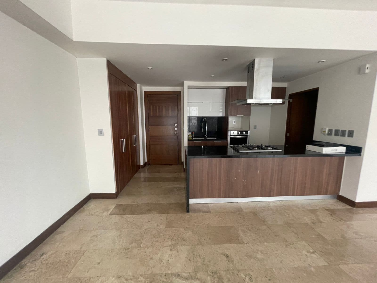 Cocina moderna con gabinetes de madera, encimeras negras, campana de acero y piso de piedra.
