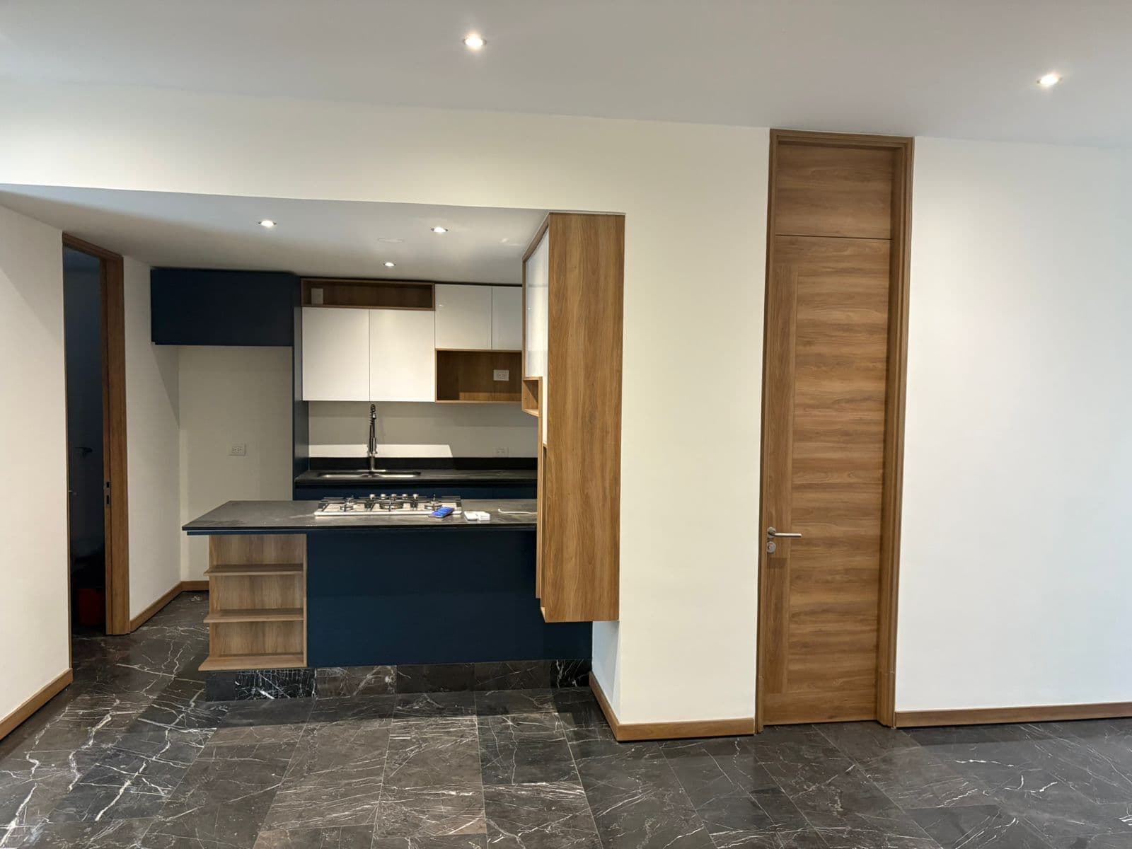 Cocina moderna con isla azul, detalles en madera y elegante suelo de mármol oscuro veteado.