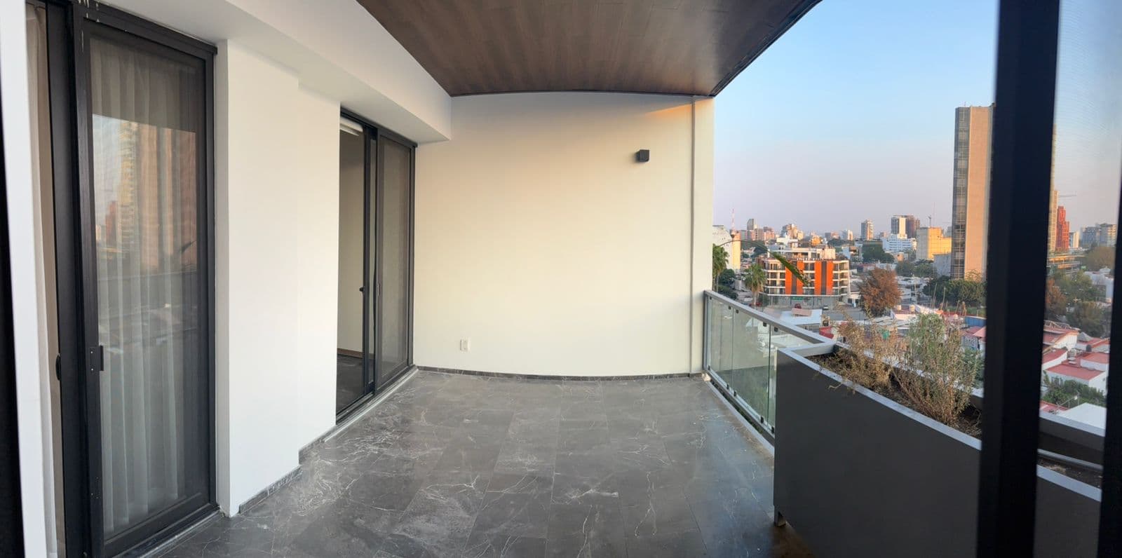 Balcón moderno con suelo de mármol gris, barandilla de cristal y vistas de la ciudad.