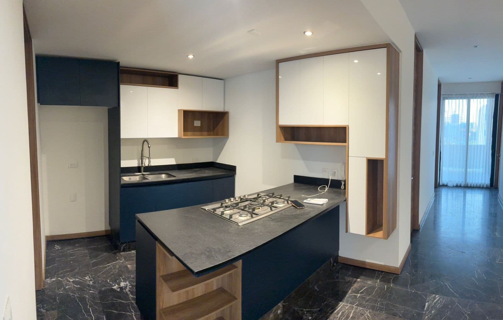 Cocina moderna con isla azul, encimera negra, armarios blancos y madera sobre mármol oscuro.