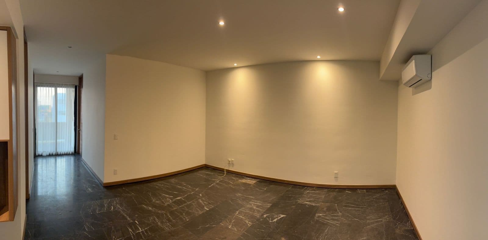 Sala moderna vacía con piso de mármol oscuro, paredes blancas, iluminación empotrada y aire acondicionado.