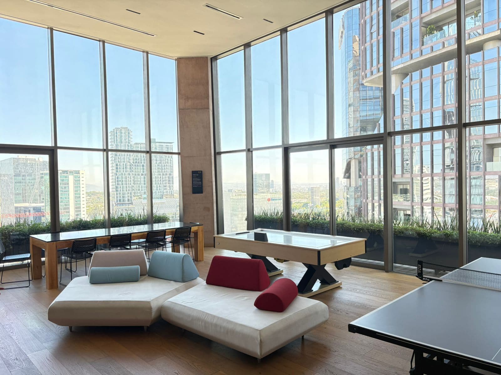Sala moderna con ventanales, sofás coloridos, mesa de billar y vistas a la ciudad.
