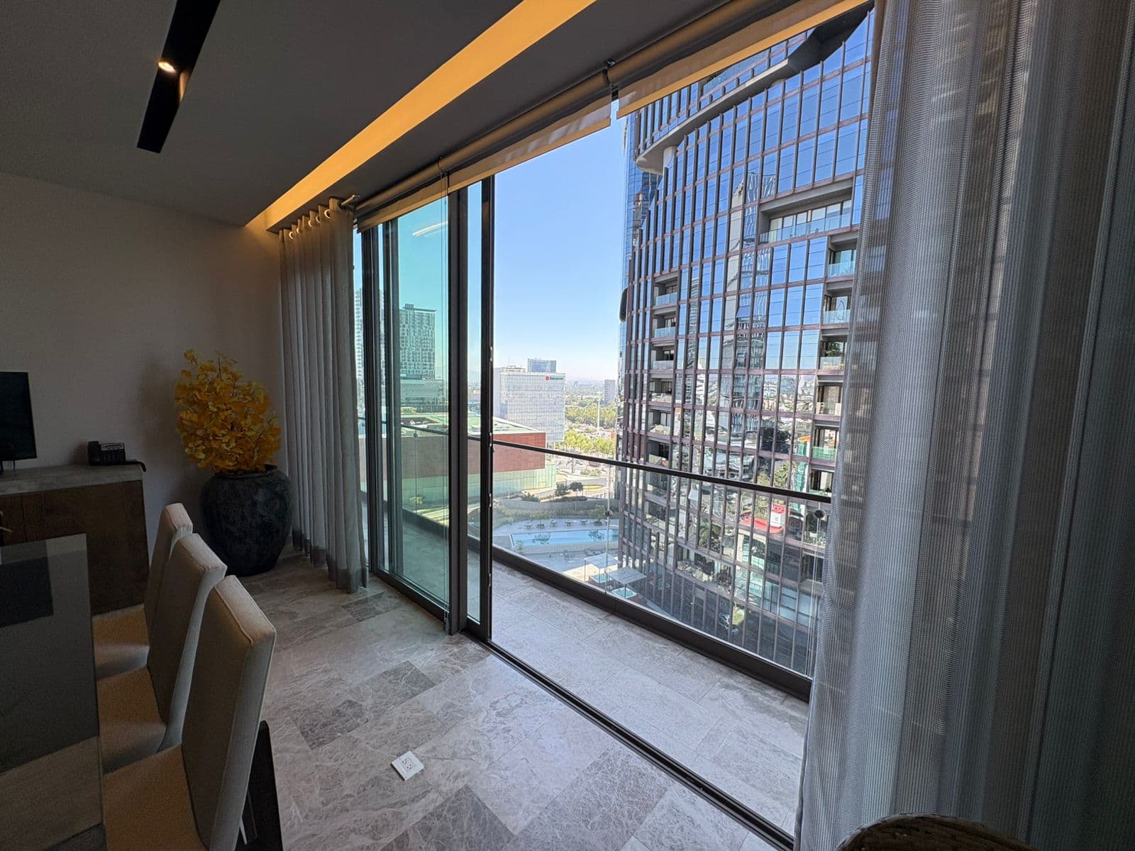 Sala moderna con suelos de mármol y balcón con vistas panorámicas a rascacielos de cristal.