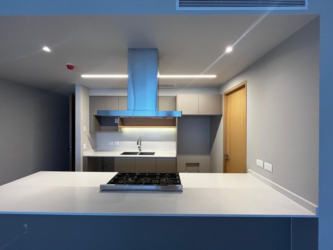 Cocina moderna con isla blanca, estufa de gas, campana de acero inoxidable y gabinetes grises.