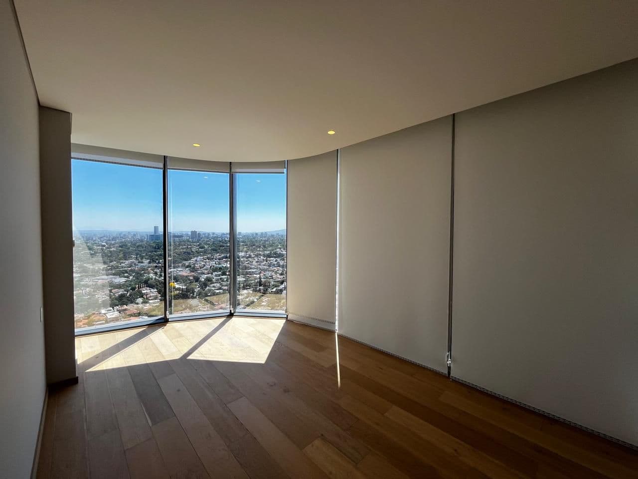 Habitación vacía con piso de madera y ventanales con vista panorámica a la ciudad.