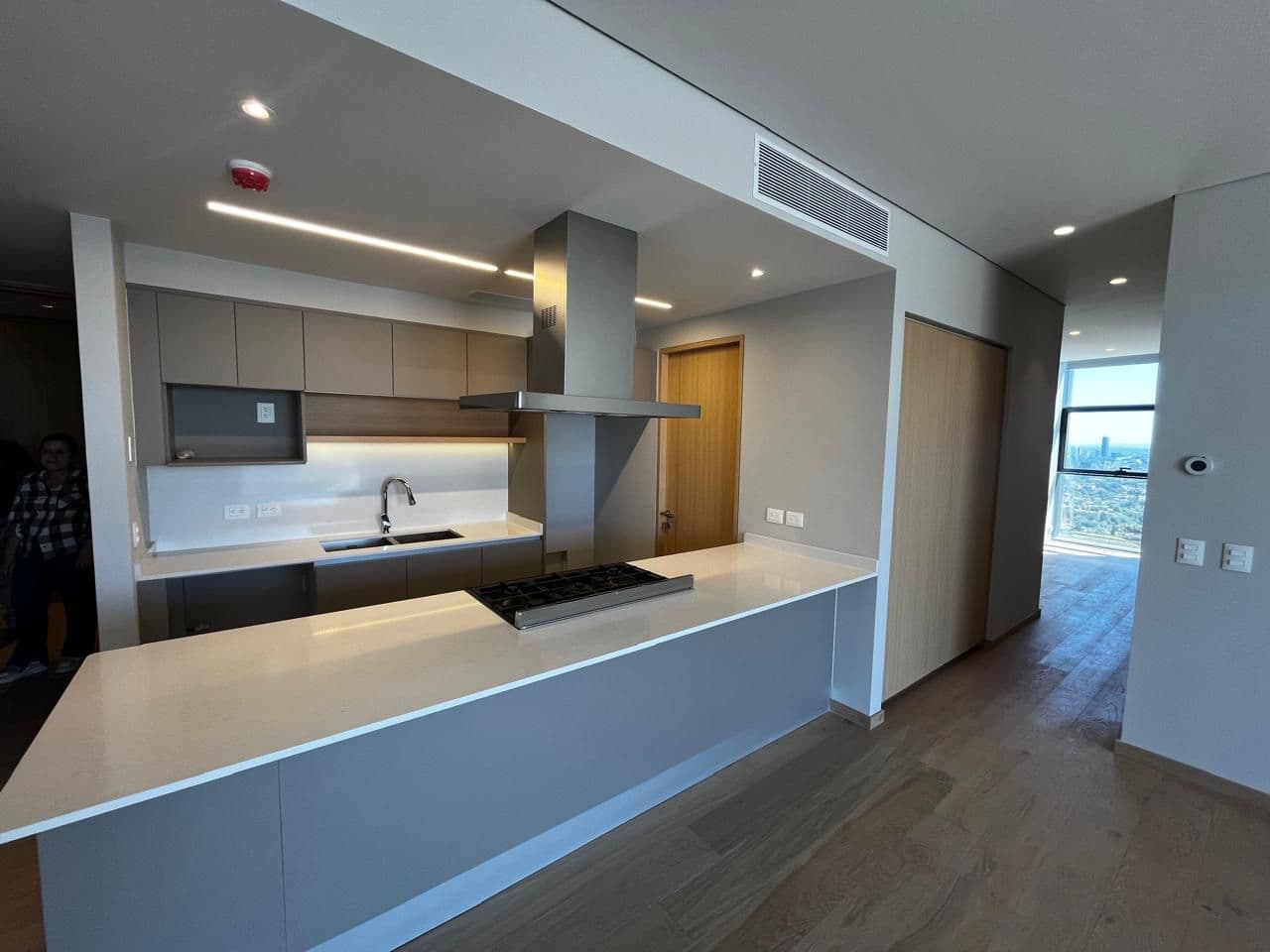 Cocina moderna con isla blanca, campana de acero, gabinetes grises y suelos de madera.