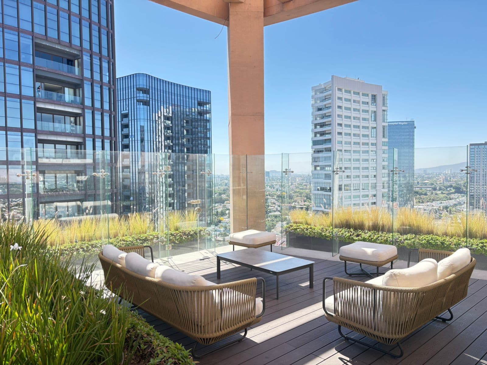 Terraza moderna con sofás blancos, mesa de centro y vistas panorámicas a rascacielos urbanos.