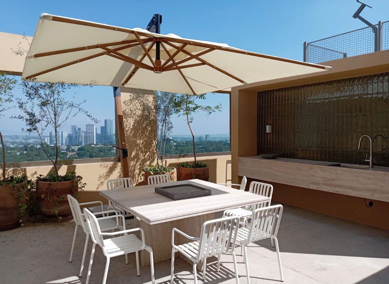 Terraza moderna con sombrilla blanca, mesa de piedra y vista panorámica al horizonte urbano.
