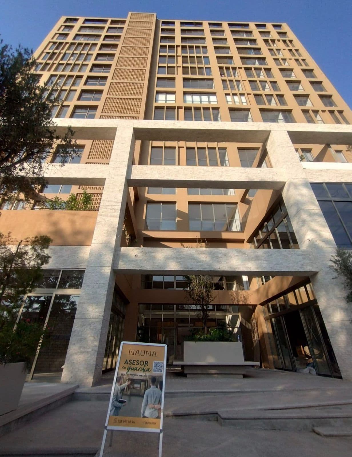 Edificio moderno color arena con vigas blancas y letrero de Nauna frente a la entrada.