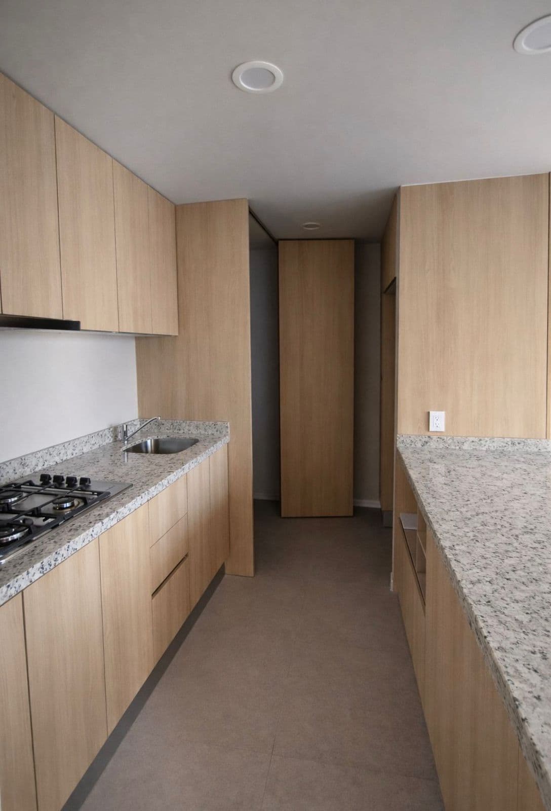 Cocina moderna con gabinetes de madera clara, encimeras de granito moteado y estufa de gas.